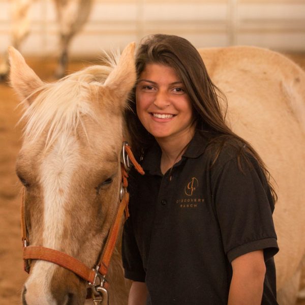 A teenage girls smiles at the camera while doing equine therapy at an equine residential treatment center | Discovery Ranch South