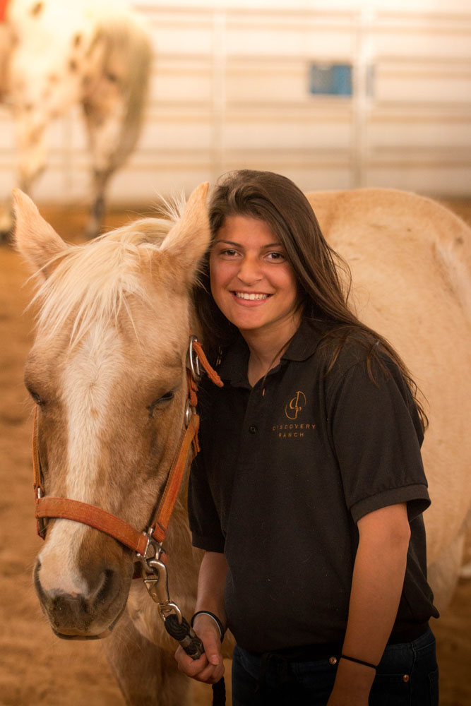A teenage girl smiles at the camera while participating in an equine therapy program at Discovery Ranch South, a residential treatment center for teenage girls and adolescents assigned female at birth